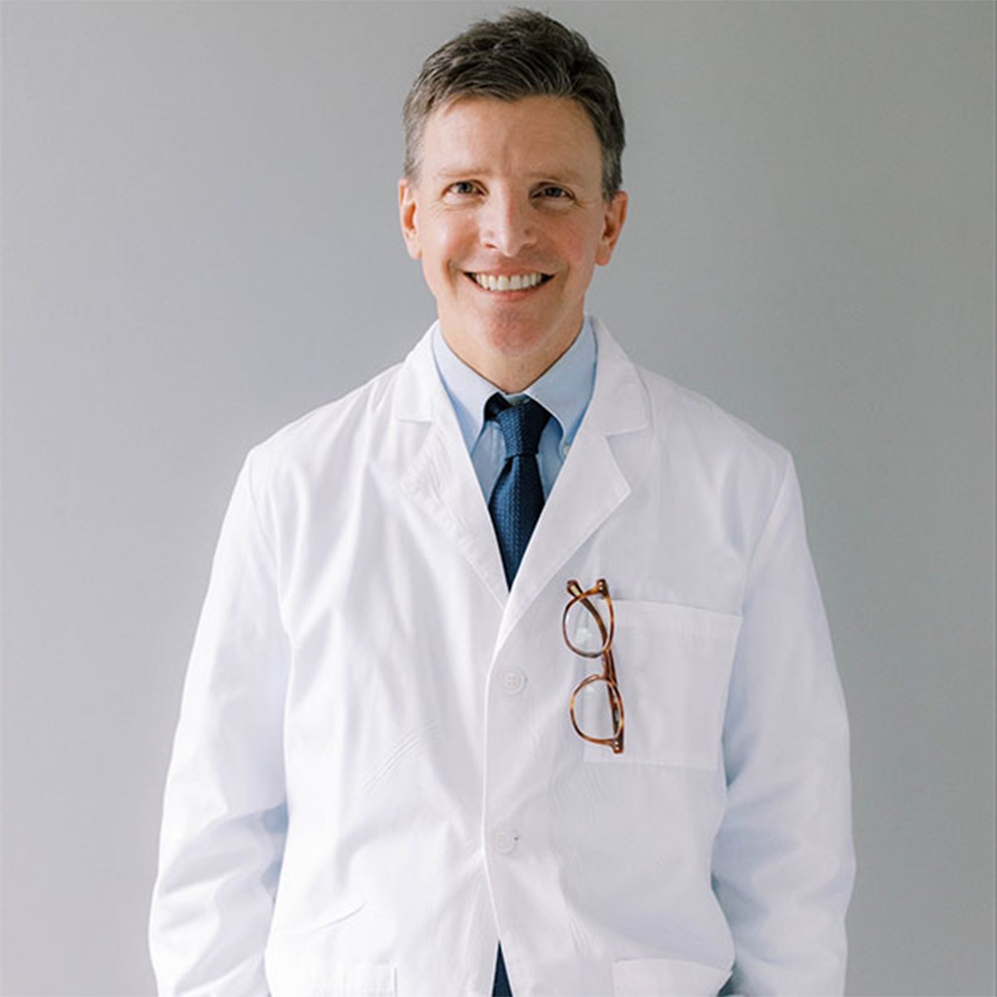 Dr. Jeff Berndt, board-certified orthodontist in white coat, smiling, with glasses hanging from pocket, representing personalized orthodontic care in Chapel Hill.